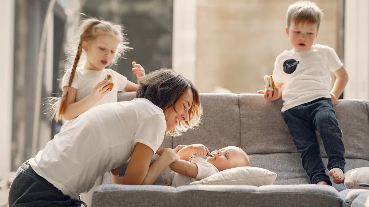 Side view of woman playing with toddler while other children standing nearby in living room